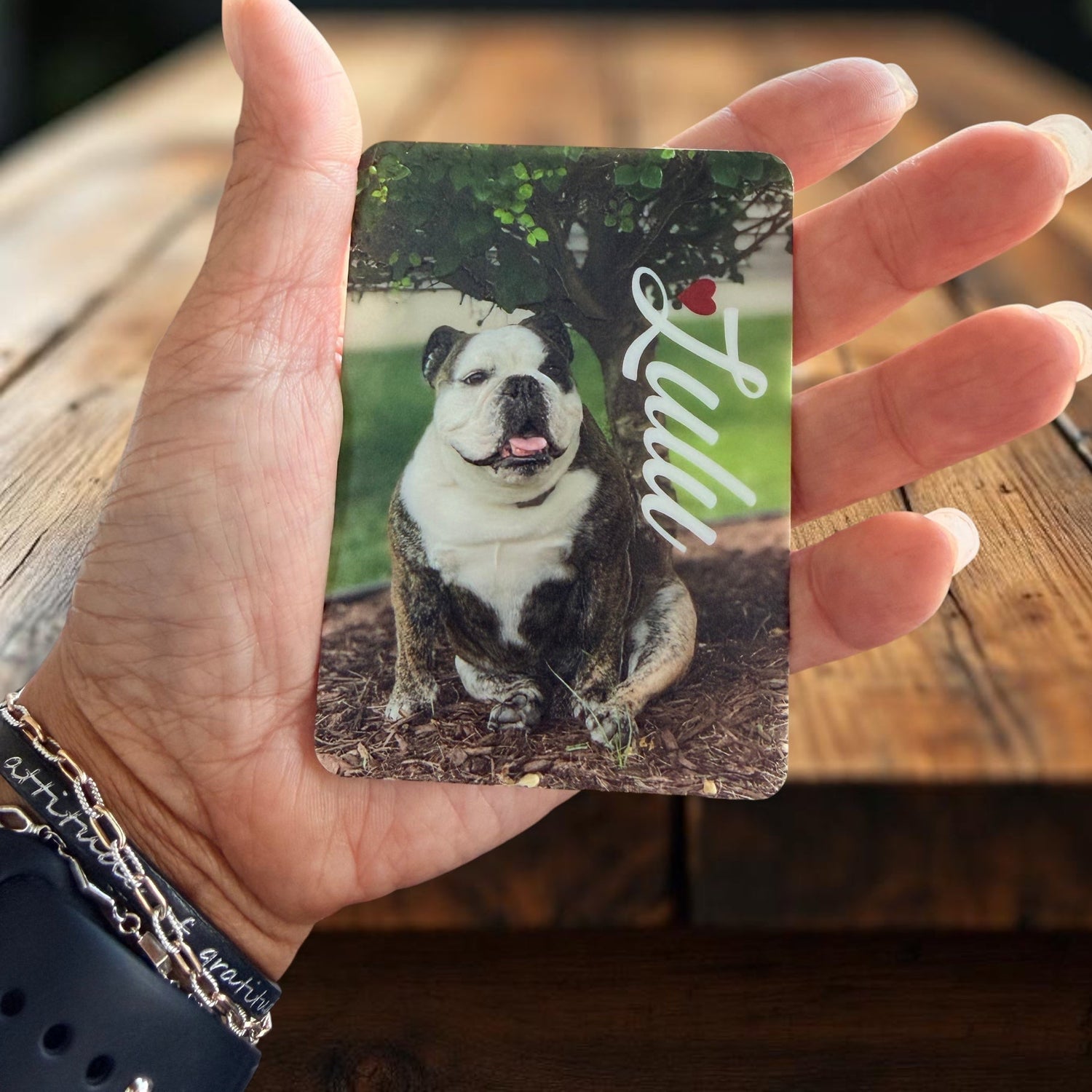 Hand holding a card with a bulldog picture and 'Lulu' text on a wooden surface